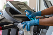 Staff using wet wipe and a blue sanitizer from the bottle to clean treadmill in gym. Antiseptic,disinfection ,cleanliness and healthcare, Anti Corona virus (COVID-19).