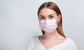 Studio portrait of young woman wearing a face mask, looking at camera, close up, isolated on gray background. Flu epidemic, dust allergy, protection against virus. City air pollution concept