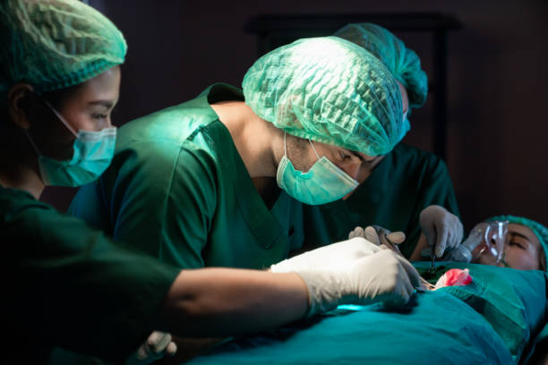 surgeons operating patient for breast implant. team of doctors are in scrubs at operating room. - cirurgia plástica - fotografias e filmes do acervo