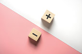 The concept of opposites, wood blog with plus and minus on white and pink background.