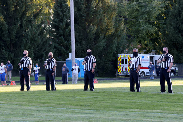 The officials on the field during the national anthem wearing mask between the Ida Bluestreaks and the Clinton Redskins on September 18, 2020 in...