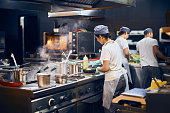 the team of cooks backs in the work in the modern kitchen, the workflow of the restaurant in the kitchen. Copy space for text