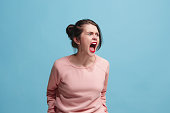 The young emotional angry woman screaming on blue studio background