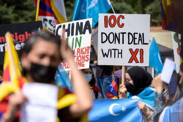Tibetan and Uyghur activists hold placards and flags during a protest against Beijing 2022 Winter Olympics in front of the Olympics Museum in...