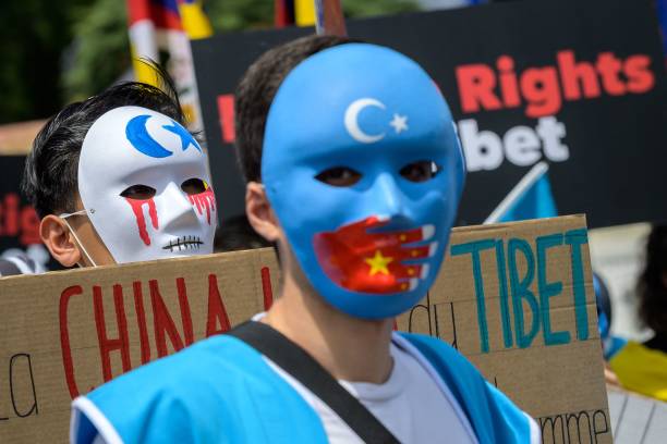 Tibetan and Uyghur activists wear masks during a protest against Beijing 2022 Winter Olympics in front of the Olympics Museum in Lausanne on June 23,...