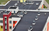 Top view dark flat roof with air conditioners and hydro insulation membranes on top of a modern apartment building residential area.
