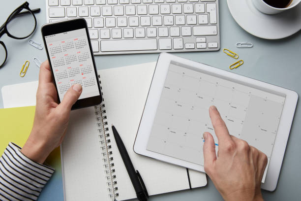top view of woman holding smartphone and tablet with calendar on desk - calendar stock pictures, royalty-free photos & images