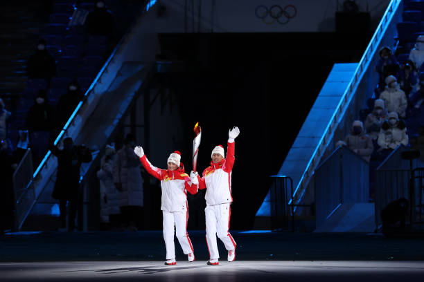 Torch bearers Dinigeer Yilamujiang and Jiawen Zhao of Team China hold the Olympic flame during the Opening Ceremony of the Beijing 2022 Winter...