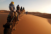 Tourists on train of camels in Sahara led by guide