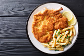 Traditional Italian veal Milanese with lemon and French fries close-up. horizontal top view