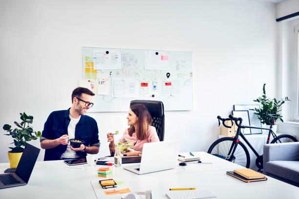 two colleagues talking during lunch break in office - professional software developer stock pictures, royalty-free photos & images