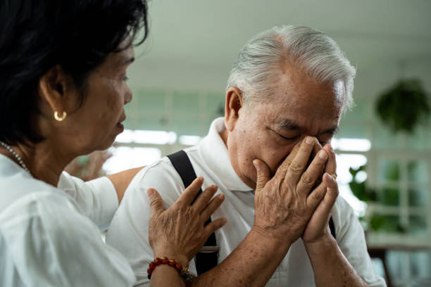 unhappy retired asian senior couple sitting on the sofa while elderly wife comforting her sad husband at home. - sad old asian couple stock pictures, royalty-free photos & images