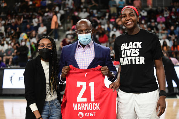 Vice President Renee Montgomery and Elizabeth Williams of the Atlanta Dream present Reverend Raphael Warnock with a Atlanta Dream jersey during the...