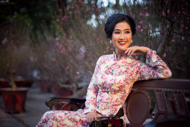 Vietnamese woman wearing Classic Ao dai sitting beside Peach blossom flowers