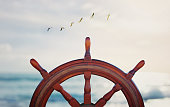 vintage nautical detail of a steering wheel of a ship in front of the sea at sunset