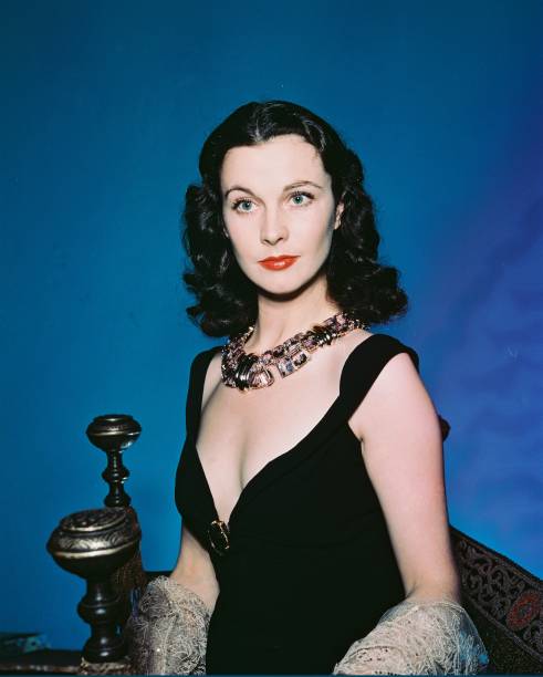 Vivien Leigh , British actress, wearing a black dress with a plunging neckline, and an ornate necklace, in a studio portrait, against a blue...