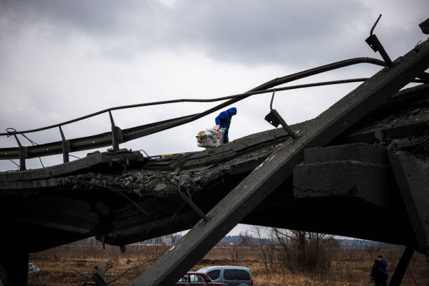 Volunteer pulls a trolley with food on a destroyed bridge near the city of Irpin, northwest of Kyiv on March 13, 2022. - Russian forces advance ever...