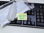 Welcome back note with hand sanitizer and mask on top of keyboard