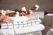 Well groomed woman hands holding the cotton branch with pile of folded bed sheets and blankets