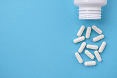 White capsules falling from the white  bottle on blue paper background. Concept of pharmacy