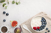 White fermented yogurt with blueberry, figs, chia seeds and raspberry in bowl on light gray table