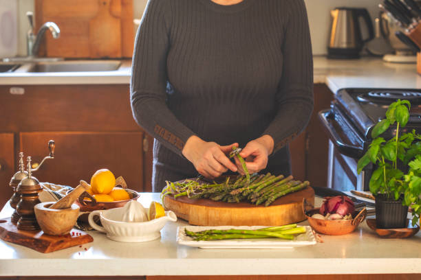 Woman cooks asparagus. Fresh asparagus and lemons on kitchen table.