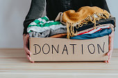 Woman holding cardboard donation box full with folded clothes.