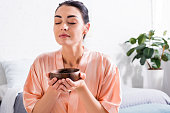 woman in silk bathrobe with wooden bowl in hands having tea ceremony in morning at home