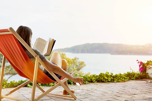 woman reading book while relaxing on deck chair - self care stock pictures, royalty-free photos & images