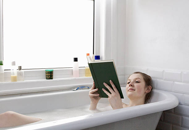 woman relaxing at home reading a book in the bath - take a bath stock pictures, royalty-free photos & images