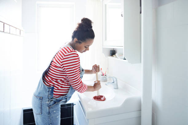 woman unclogging sink with plunger in bathroom - ralo - fotografias e filmes do acervo