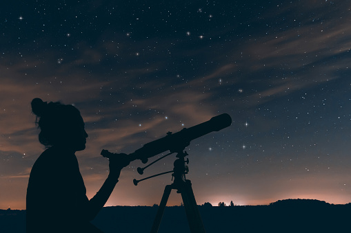 Woman with astronomical telescope. Night sky, with clouds and constellations 619655770