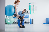 Woman with orthopedic problem exercising with ball while physiotherapist supporting her
