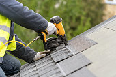 Workman using pneumatic nail gun install tile on roof of new house under construction