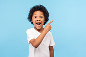 Wow look, advertise here! Portrait of amazed cute little boy with curly hair pointing to empty place