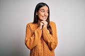 Young beautiful brunette woman wearing casual sweater over isolated white background laughing nervous and excited with hands on chin looking to the side