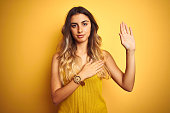Young beautiful woman wearing t-shirt over yellow isolated background Swearing with hand on chest and open palm, making a loyalty promise oath