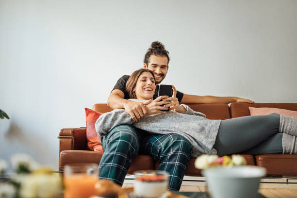 young couple with smart phone relaxing on sofa - couple lying stock pictures, royalty-free photos & images