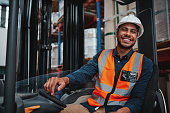 Young forklift driver sitting in vehicle in warehouse smiling looking at camera