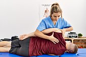 Young hispanic physioterapist woman make back rehab treatment to man at the clinic.