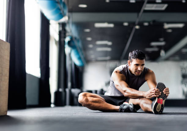 young man doing leg stretches in the gym - workout men stock pictures, royalty-free photos & images