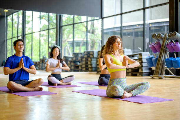 young people in yoga class sitting on mats stretching arms in a fitness studio. - international yoga day stock pictures, royalty-free photos & images