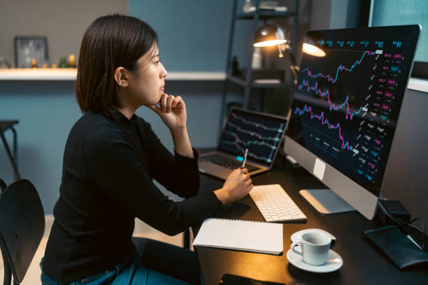 young woman doing cryptocurrency business trading on her computer at home at nigh - cryptocurrency stock pictures, royalty-free photos & images