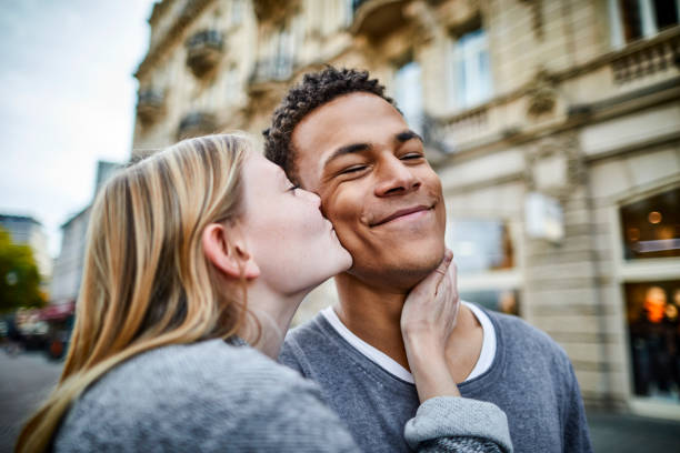 young woman kissing boyfriend in the city - love stock pictures, royalty-free photos & images