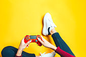 Young woman playing with two gamepads on yellow.