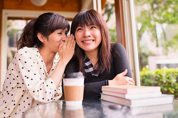 young woman whispering into other womans ear - asian woman talking hearsay stock pictures, royalty-free photos & images