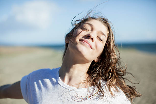 young woman with eyes closed smiling on a beach - saúde e vitalidade - fotografias e filmes do acervo