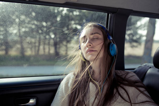 young woman with windswept hair in a car wearing headphones - listening to music in car stock pictures, royalty-free photos & images