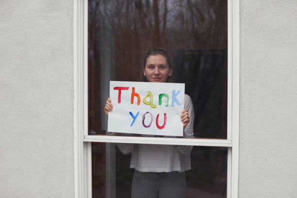 young women holding up thank you sign in window looking out - thank you stock pictures, royalty-free photos & images