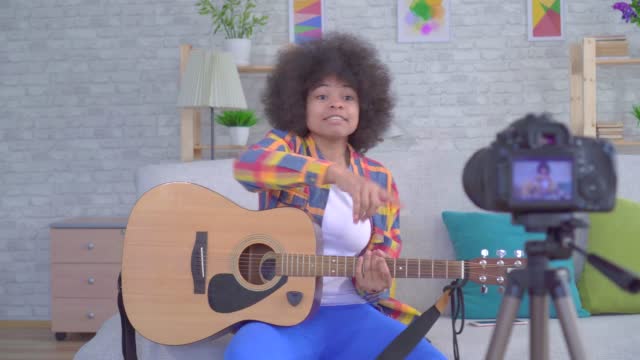 African american woman blogger with an afro hairstyle with a guitar before the camera